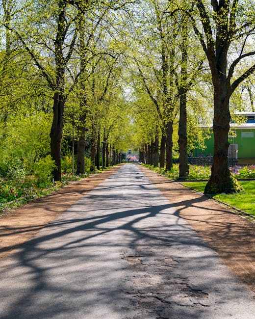 A narrow cobblestone street in Tower Hamlets lined with row houses featuring brick facades and large window panes. The front yards of these properties are landscaped with an array of potted plants, fl